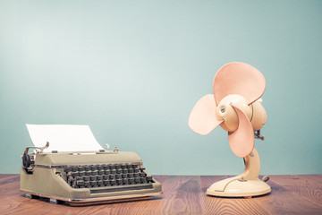 Retro classic typewriter with sheet of paper and old cooling fan on wooden table front mint green wall background. Vintage style filtered photo