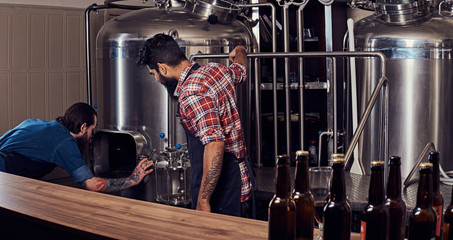 Two bearded hipster males in an apron working in a brewery factory.