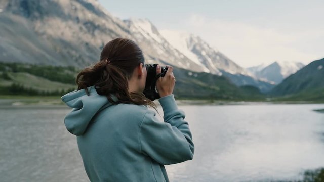 Girl takes pictures of herself against the backdrop of a beautiful mountain landscape, standing on top of a mountain. Young lady hiker standing on top of the mountain and taking a picture of valley.