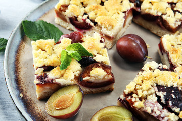 Rustic plum cake on wooden background with plums around.