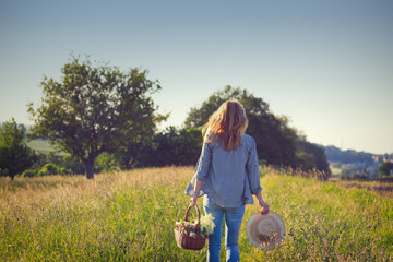 Woman holding straw hat and wicker basket is walking in nature, harvest flowers for alternative...