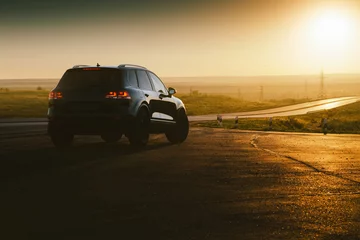Foto op Canvas Black car is parked at countryside asphalt road near highway at golden sunset © Ivan Kurmyshov