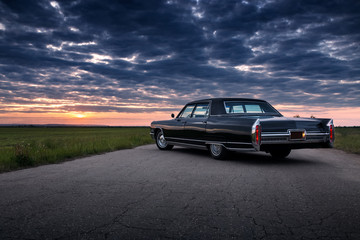 La voiture de muscle vintage rétro noire est garée sur la route goudronnée de campagne au coucher du soleil doré