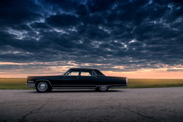 Fototapeta na wymiar Black retro vintage muscle car is parked at countryside asphalt road at golden sunset