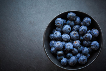 fresh blueberries in a black Bowl on a dark concrete background