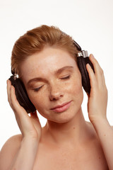 Fototapeta premium Young beautiful woman with freckles and wireless earphones on her ears. studio shot, isolated over white background.