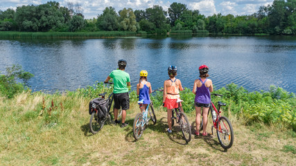 Naklejka premium Family on bikes cycling outdoors, active parents and kids on bicycles, aerial view of happy family with children relaxing near beautiful river from above, sport and fitness concept 