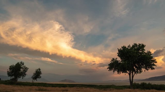 Vibrant sunset time lapse looking past trees on the horizon over Utah Lake.