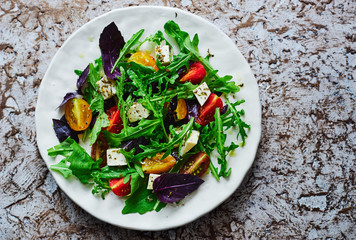 Fresh salad with vegetables, arugula and feta cheese in a plate top view
