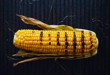 Delicious homemade hot grilled corn cob on black wooden background top view 