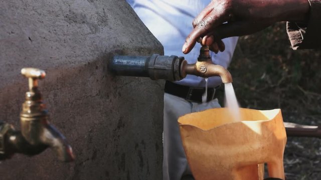 Close up of body part of black people getting water from a faucet at water point in africa
