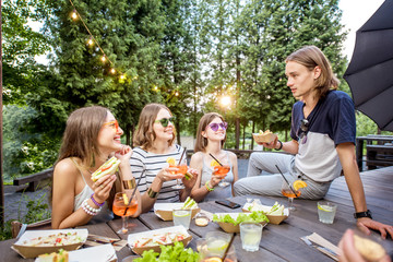 Young friends having fun sitting together with tasty snacks and drinks during the evening lights at the park cafe outdoors