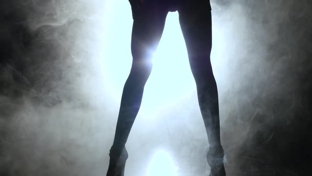 Woman is dancing a sexy dance in the smoke. Black background. Silhouette
