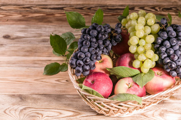 Ripe red apples with leaves, black and white grapes in a basket. Autumn harvest. Close-up.