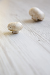 Raw champignon mushrooms, side view. White wooden background. Close-up.