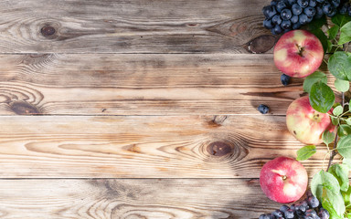 Ripe red apples with leaves and grapes on a wooden background. Autumn harvest. Top view. Copy space