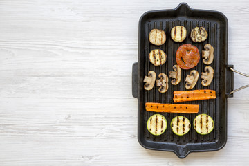 Top view, grilled vegetables in a grilling pan on a white wooden table. From above, flat lay, overhead.