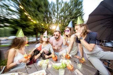 Happy friends having fun together celebrating birthday at the outdoor park cafe during the evening light. Motion blur image technic
