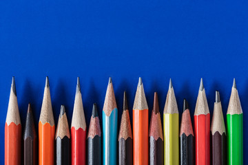 Top view of colorful various pencils placed in row on blue background
