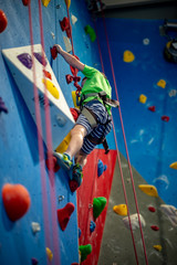 Young boy climbing up on practice wall in indoor rock gym