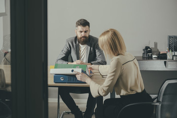 Businessman and businesswoman sit at office desk. Bearded man and woman have business meeting. Concentration at work. Communication and cooperation with colleagues. Work process concept