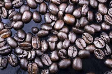 Brown coffee beans on black surface. Top view close up.