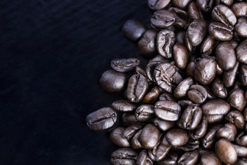Brown coffee beans on black surface. Top view close up.