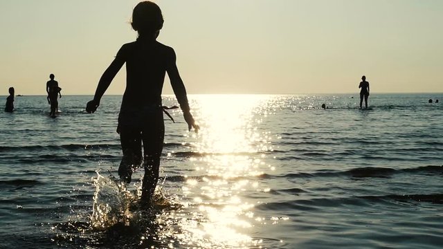Child runs in the sea water in sun flare, kid silhouette running in the sea. Little girl having fun on sea shore. Slow motion