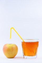 Fresh juice in a transparent glass and apple, fresh fruit juice on a white background, yellow cocktail tube in a healthy drink, healthy lifestyle, vegetarian drink, isolated