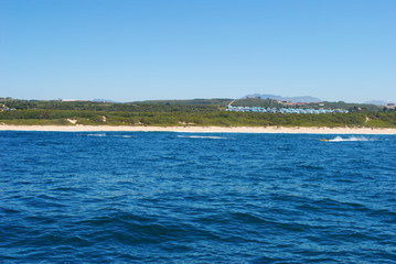 Ocean view of a line of houses with blue roofs sitting on the horizon above a beach in Mossel Bay, 2012
