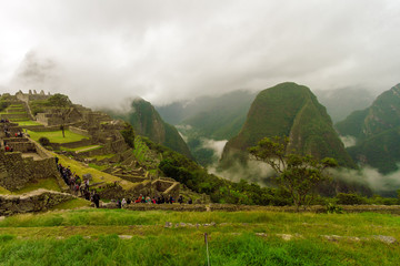 Fototapeta premium Machu Picchu, Peru - February 12, 2018: Group of tourists moving along a path in their visit to the ruins of Machu Picchu during a cloudy morning
