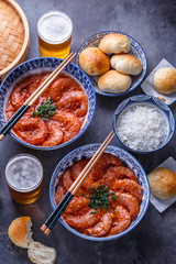 Spicy asian shrimps in tomato sauce with rice, buns and beer, top view