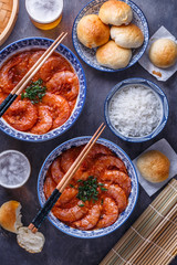 Spicy asian shrimps in tomato sauce with rice, buns and beer, top view