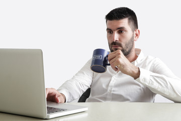 Young businessman drinking his coffee in front of laptop, studio shot, office life