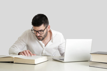 
Studio portrait of young man reading a book in front of his laptop