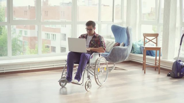 Disabled man in wheelchair with laptop in his apartment.