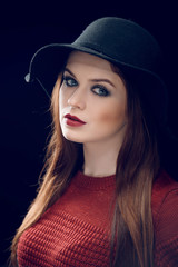 Studio portrait of young attractive woman with brunette hair, beautiful make up wearing black hat posing isolated on black background. Close up