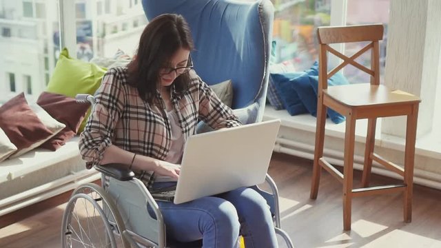 Disabled girl in wheelchair with laptop in his apartment