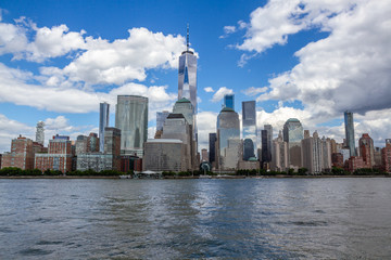 Fototapeta na wymiar View of downtown Manhattan from the water. Freedom Tower in middle of frame, white clouds in blue sky.