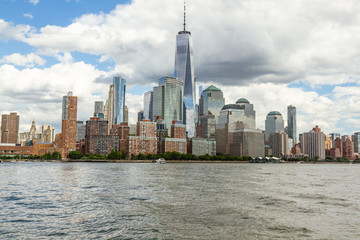 Obraz premium View of downtown Manhattan from the water. Freedom Tower in middle of frame, white clouds in blue sky.