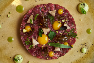 Beef tartare Steak with egg yolk, pistachios, truffle oil, green mayonnaise on porcelain plate. Classic tartare meat with ingredients. Luxury food