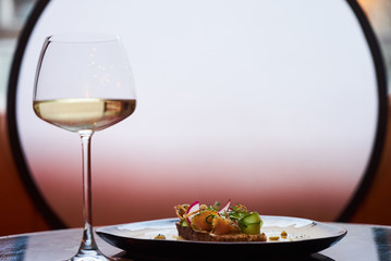 Smorrebrod Danish sandwich with salmon fish, curd mousse, marinated cucumber and radish. Delicious vegetarian snack food with dark rye bread and different topping and wine glass at restaurant table