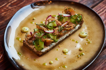 Smorrebrod Danish sandwich with salmon fish, curd mousse, marinated cucumber and radish. Delicious vegetarian snack food with dark rye bread and different topping and wine glass at restaurant table