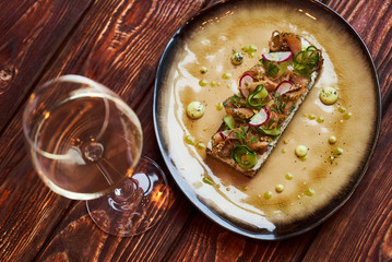 Smorrebrod Danish sandwich with salmon fish, curd mousse, marinated cucumber and radish. Delicious vegetarian snack food with dark rye bread and different topping and wine glass at restaurant table