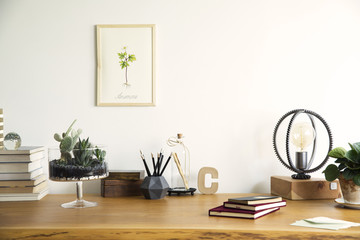 Vintage, creative home office interior with wooden desk, books, laptop, romantic illustrations of plants, table lamp and office accessories.