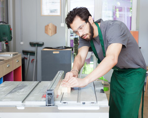 Obraz premium A carpenter works on woodworking the machine tool. Carpenter working on woodworking machines in carpentry shop. A man works in a carpentry shop. Saws furniture details with a circular saw