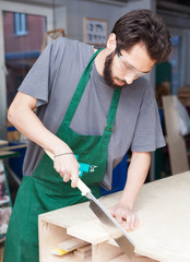 A carpenter. a young bearded hipper in a carpentry workshop saws a steep Japanese saw