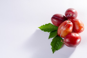 Group of ripe oval Victoria plums from England on white background with leaves