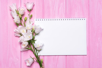 White flowers bells and an empty notebook for your text on a pink wooden background.