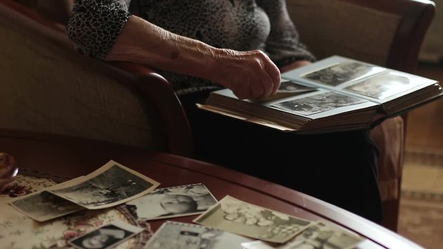 The old woman is looking at old photographs of the house, close-up. nostalgia and loneliness
